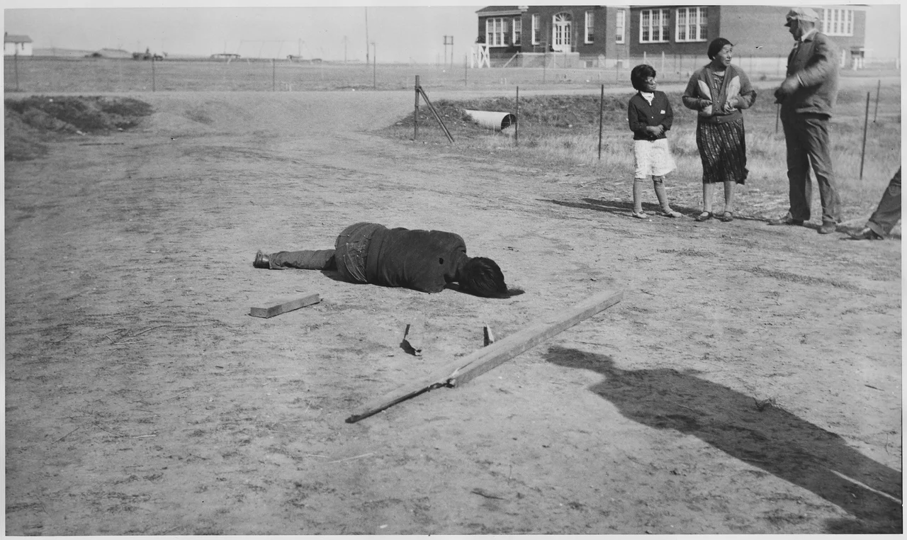 Scope and content: The body is sprawled on ground; girl, woman, and man standing by.